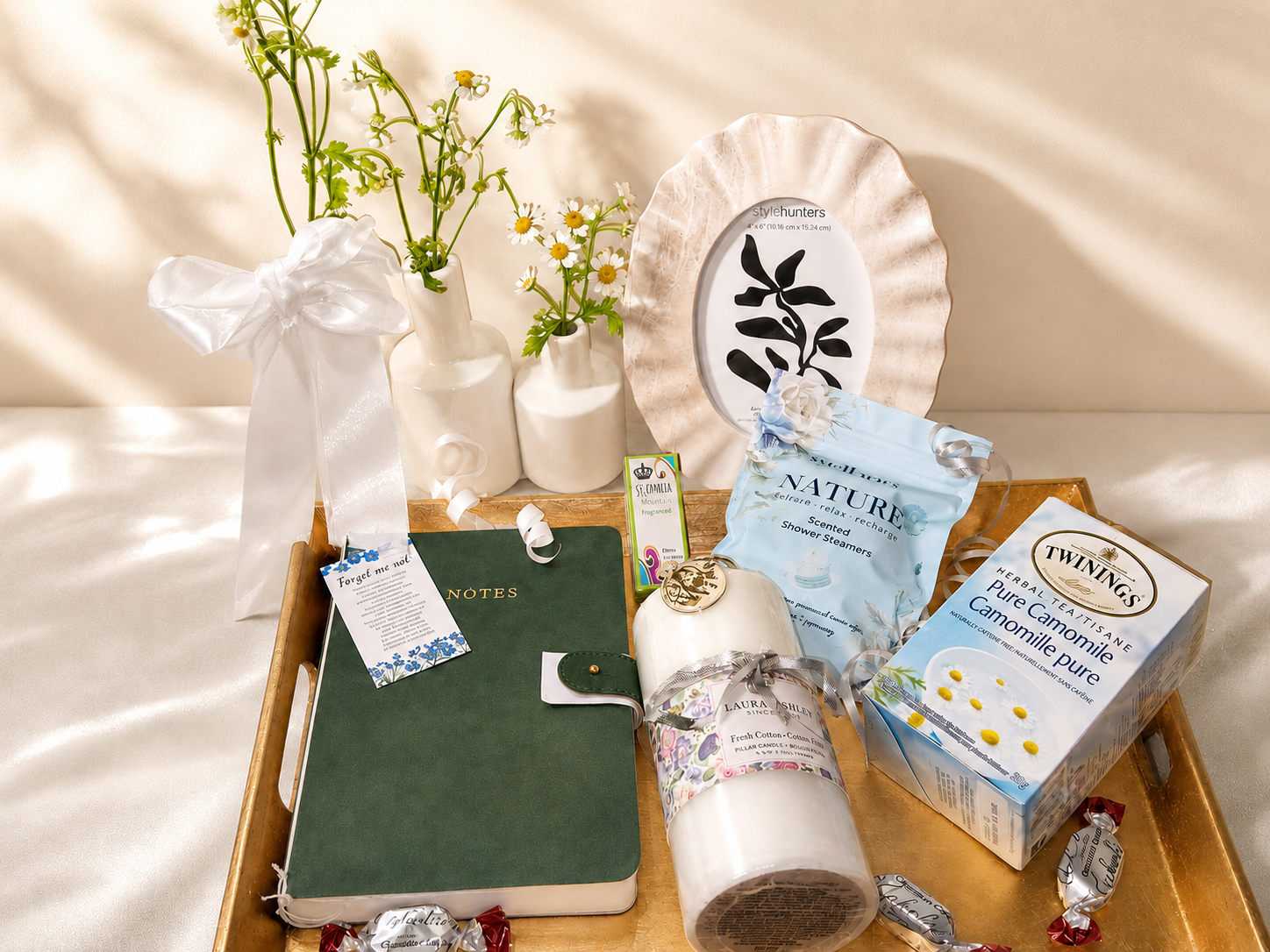Editorial flat-lay of bereavement basket items — candle, journal, tea, daisies